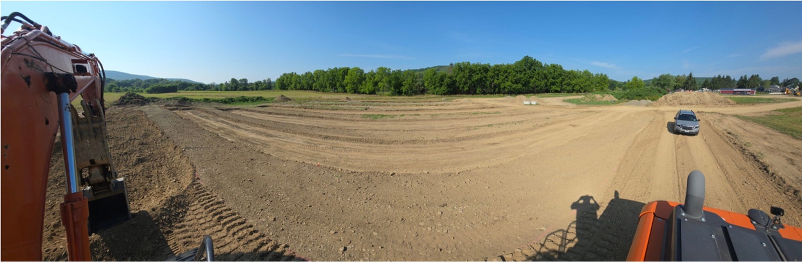 Excavator grading the Phase 1 site on Route 28 under a clear sky